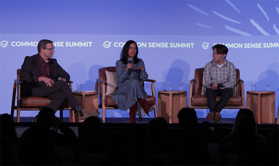 Three adults seated on stage against a blue backdrop