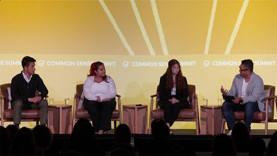 Four panelists seat on stage in front of yellow screen